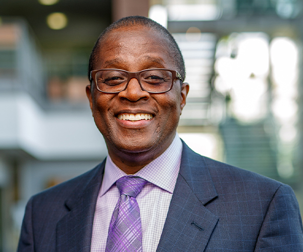 Smiling male business professional wearing glasses, navy suit and purple tie.