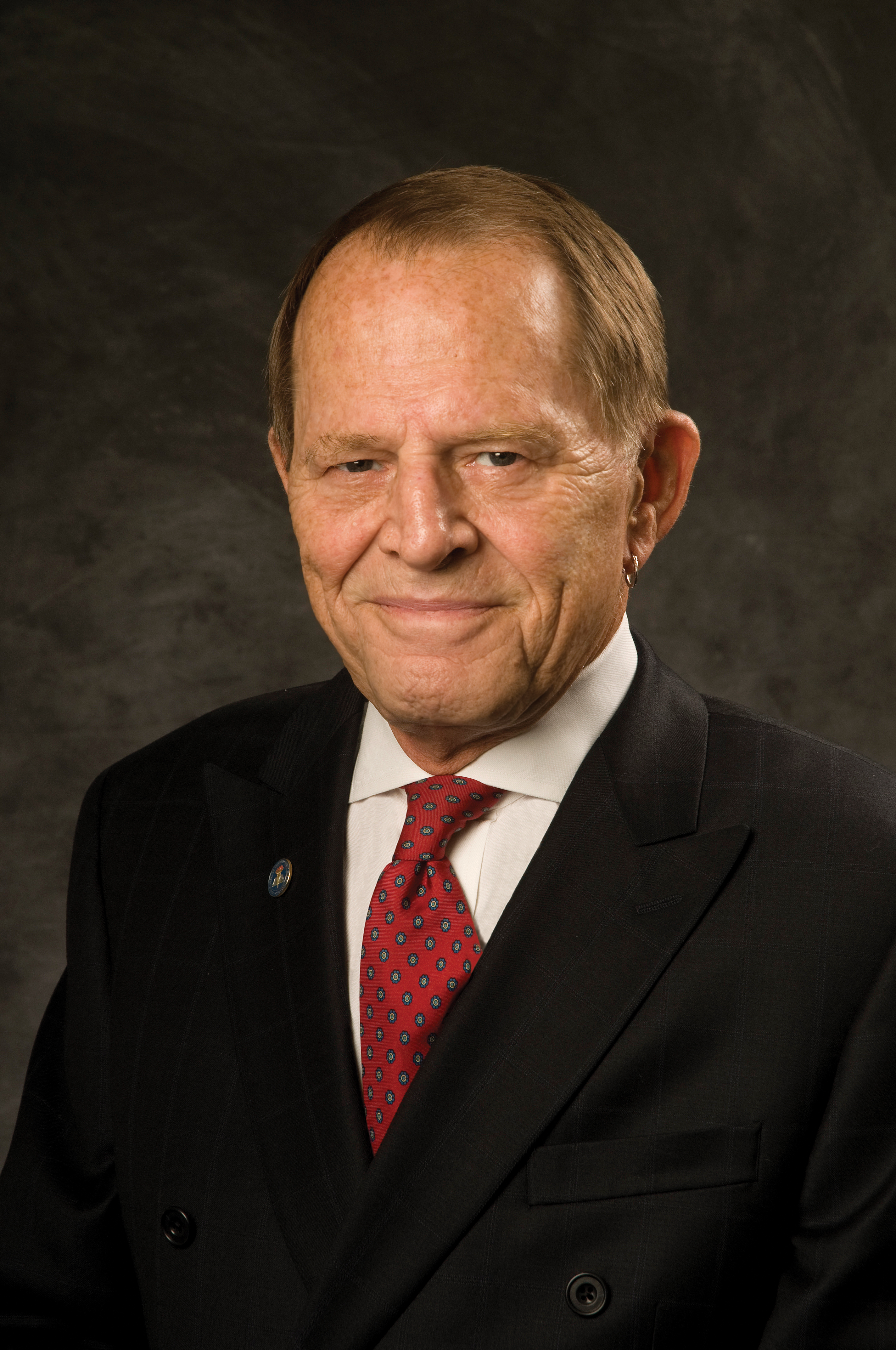 Owner and Chairman Dr. Joseph T. Wells dressed in black suit and red tie and smiling.